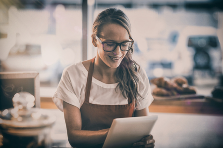 Smiling waitress sitting at table and using digital tablet in cafeの写真素材