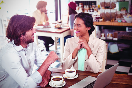 Smiling man and woman using a laptop while having cup of coffee in cafeの写真素材