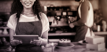 Portrait of smiling waitress using digital tablet at counter in cafÃÂ©の写真素材