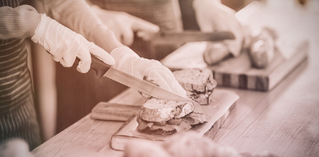 Mid-section of waiter chopping bread roll and sandwich on chopping board in cafÃÂ©の写真素材
