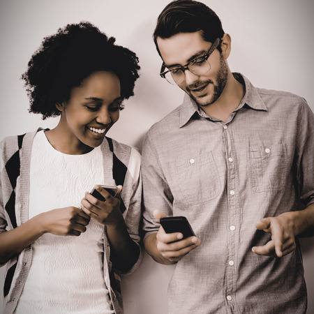 Man and woman standing against white wall and using mobile phone in officeの写真素材
