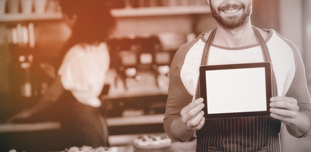 Portrait of smiling waiter showing digital tablet at counter in cafÃÂ©の写真素材