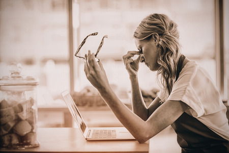 Tired waitress sitting at table and using laptop in cafÃƒÂ©