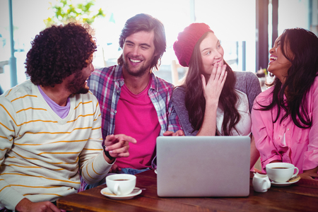 Laughing friends enjoying coffee with laptop in cafeの写真素材