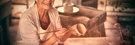Portrait of female potter painting on bowl in pottery workshopの写真素材