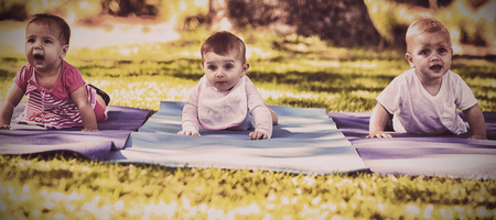 Three babies crawling on exercise-mat in park