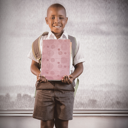 Happy schoolkid holding books and standing in classroom at schoolの写真素材