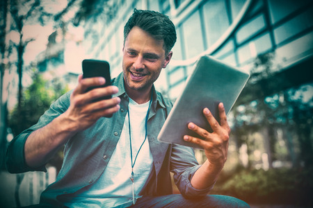 Low angle view of business executive using mobile phone and digital tablet outside office
