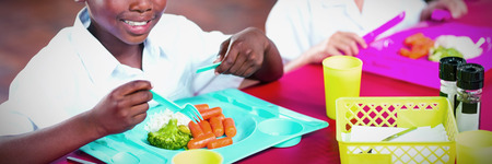 Portrait of boy and girl in school uniforms having lunch in school cafeteria