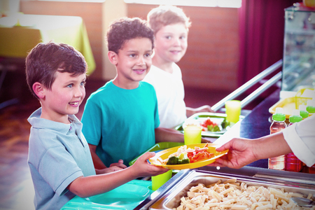Cropped image of woman serving food to smiling schoolchildren in canteenの写真素材