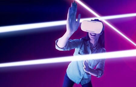 Woman gesturing while using virtual reality headset against turquoise and purple background