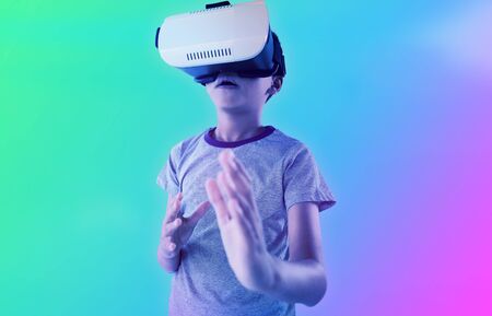 Boy gesturing while using virtual reality headset against turquoise and purple backgroundの写真素材