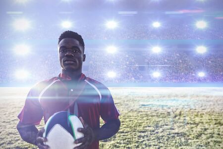 Rugby player holding football at field. against digital image of crowded soccer stadium