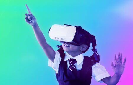 School girl pointing while using virtual reality headset against turquoise and purple background