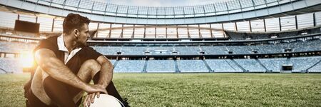 Rugby player sitting on the field with football. against rugby stadium at dawnの写真素材