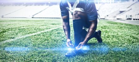 Front view of African american male rugby player tying shoelaces in the stadiumの写真素材