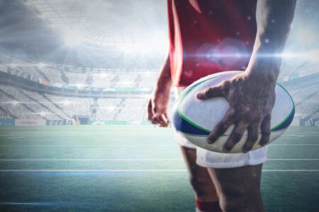 Rugby player holding rugby ball against stadium against skyの写真素材