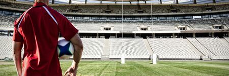 Male rugby player holding rugby ball  in the ground against rugby goal post on a sunny day in the stadiumの写真素材