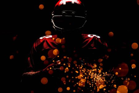 American football player standing in rugby helmet and holding rugby ball against firework bursting sparkle backgroundの写真素材