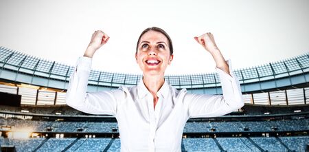 Successful businesswoman with clenched fists looking up against rugby stadium at dawnの写真素材