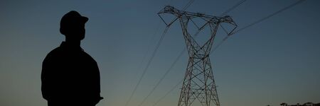 Supervisor writing notes on clip board against the evening electricity pylon silhouette