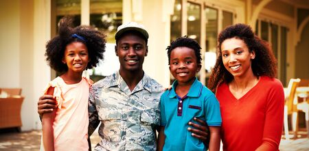 Portrait of a young adult African American male soldier in the garden outside his home, kneeling with his arms around his young son and daughter, his mixed race wife beside them, all smiling to cameraの写真素材