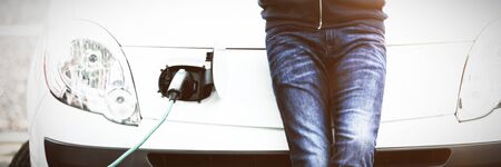 Mid section of man using mobile phone while charging electric car at charging station