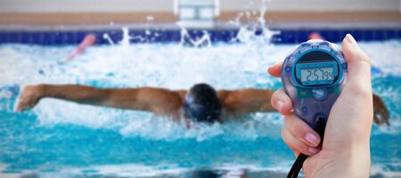 Close-up of a woman holding a chronometer to measure performance against swimmer swimming in the...