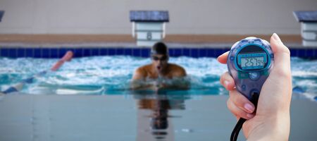 Close-up of a woman holding a chronometer to measure performance against swimmer swimming in the...