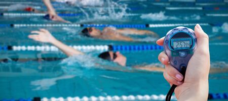 Close-up of a woman holding a chronometer to measure performance against swimmers swimming in the...