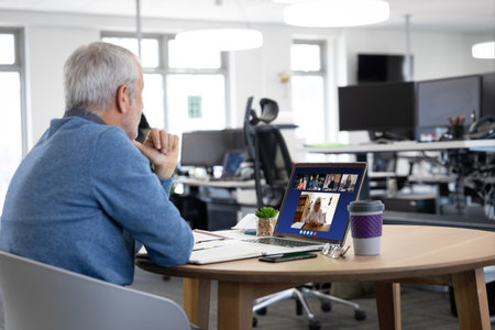 Caucasian man in office having video call with colleagues displayed on laptop screen. social distancing communication technology workplace during covid 19 pandemic.の写真素材