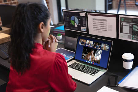 Caucasian woman in office having video call with diverse colleagues displayed on laptop screen....