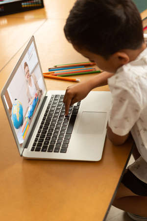 Mixed race schoolboy using laptop on video call with female teacher. Online education staying at home in self isolation during quarantine lockdown.の写真素材