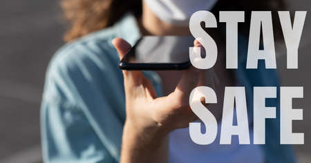The words Stay Safe with a mixed race man wearing a face mask, using a smartphone. Public health...