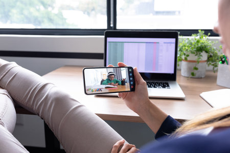 Caucasian female teacher sitting at desk using smartphone having online lesson with pupil. at home in isolation during quarantine lockdown.の写真素材
