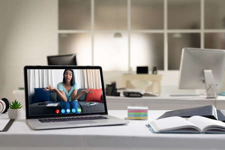 Mixed race female woman having video call on screen of laptop on desk. online meeting, working in...