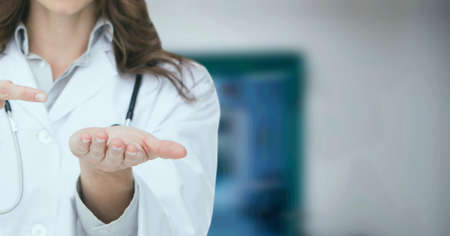 Composition of midsection of female doctor in lab coat pointing over out of focus hospital. medicine and science concept digitally generated image.の写真素材