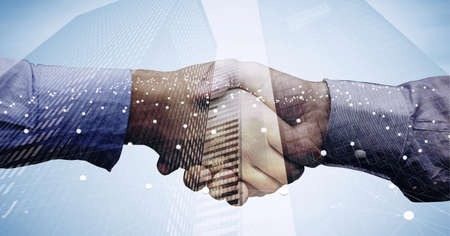 Network of connections over mid section of two businessmen shaking hands against tall buildings....
