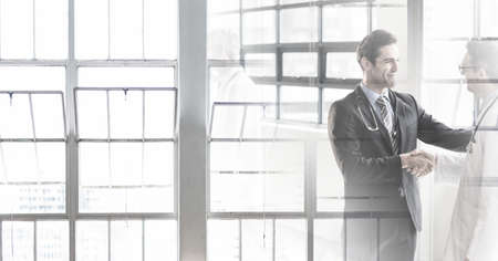 Composition of two smiling male doctors shaking hands in corridor with double exposure. healthcare, partnership and success concept digitally generated image.の写真素材