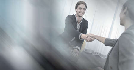 Composition of smiling businessman and businesswoman shaking hands in meeting room with motion blur....