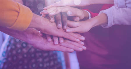 Composition of midsection of friends stacking hands with spots of light. teamwork, motivation and success concept digitally generated image.の写真素材