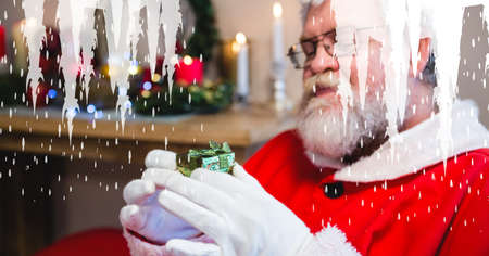 Composition of icicles over santa claus holding tiny christmas present. christmas tradition and festivity concept digitally generated image.の写真素材