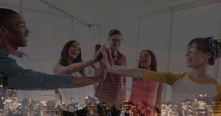 Composition of smiling office colleagues hand stacking over cityscape. teamwork, success, business and finance concept digitally generated image.の写真素材