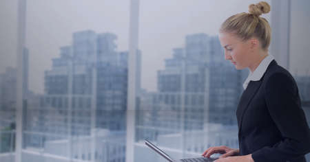 Composition of businesswoman using laptop in office over modern skyscrappers. global networks and digital interface concept digitally generated image.の写真素材