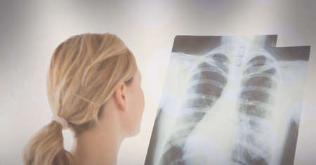 Rear view of caucasian female doctor examining x-ray report against grey background. medical...