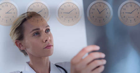 Multiple clocks over caucasian female doctor examining x-ray report against grey background. medical research and technology conceptの写真素材