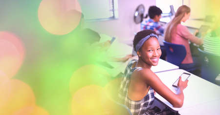Composition of light circles over african american female teenager using smartphone in classroom....