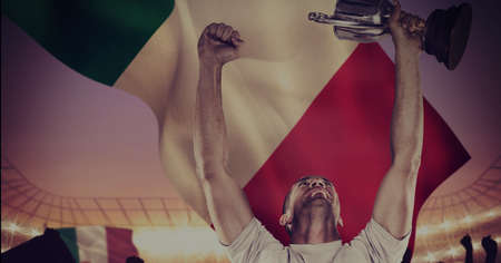 Male athlete with arms in air holding cup at sports stadium over italian flag. global sports and victory concept digitally generated image.の写真素材