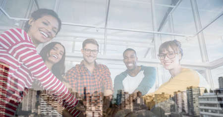 Composition of smiling office colleagues hand stacking over cityscape. teamwork, success, business and finance concept digitally generated image.の写真素材