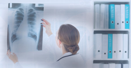 Rear view of caucasian female doctor examining x-ray report against grey background. medical research and technology conceptの写真素材